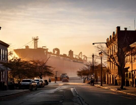 Image representing global trade impact; large ship in the background with goods looking upon a dark city.