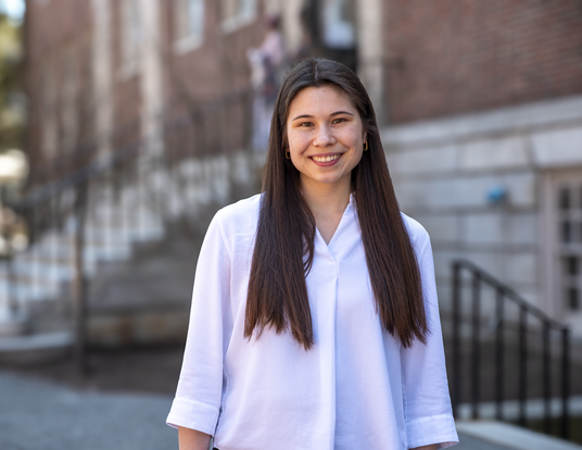 Abigail wearing a white shirt with hair down standing in front of Lehman Hall 