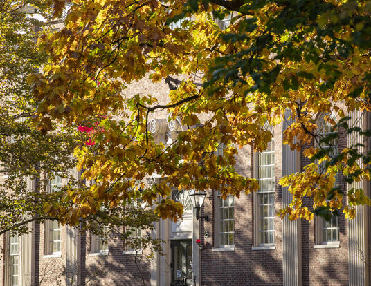 brick facade of Lehman Hall behind a tree beginning to show yellow foliage