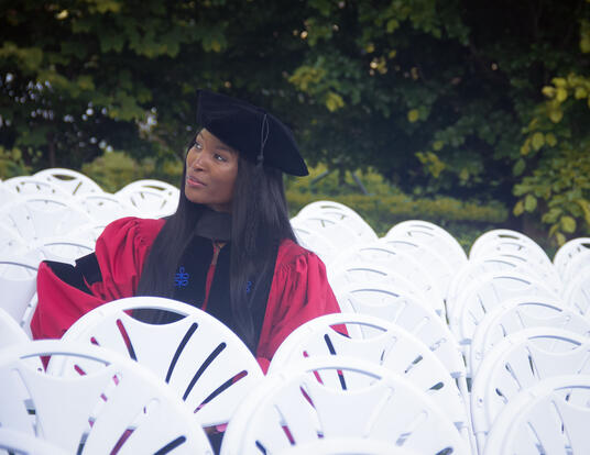 Nkem-Onyekpe sitting in a row of white chairs wearing regalia
