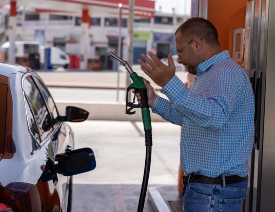 guy standing at gas pump seemingly frustrated