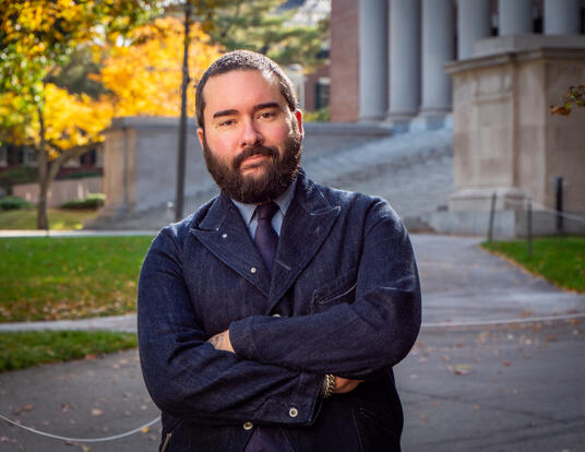 Daniel Evrard headshot; wearing a dark denim jacket standing in front of Widener Library