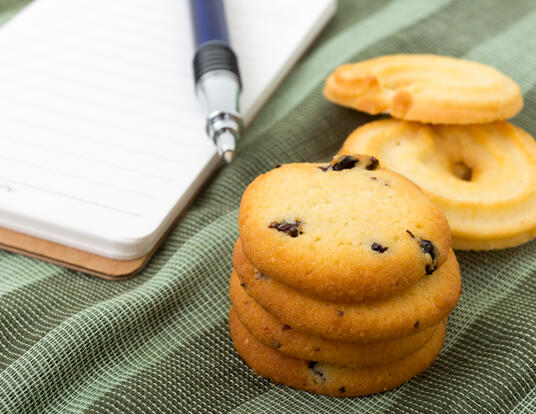 stack of chocolate chip cookies next to a pen and pad of paper