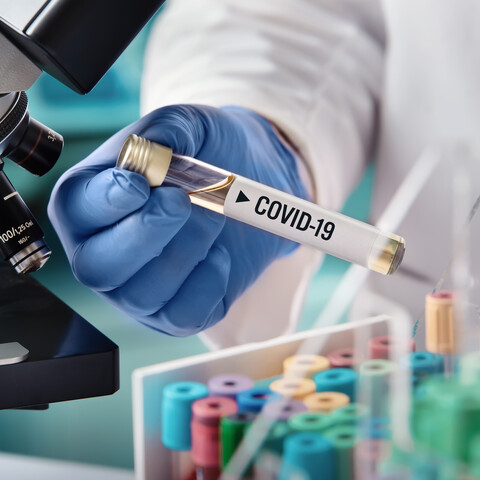 COVID-19 vial being held in lab next to microscope