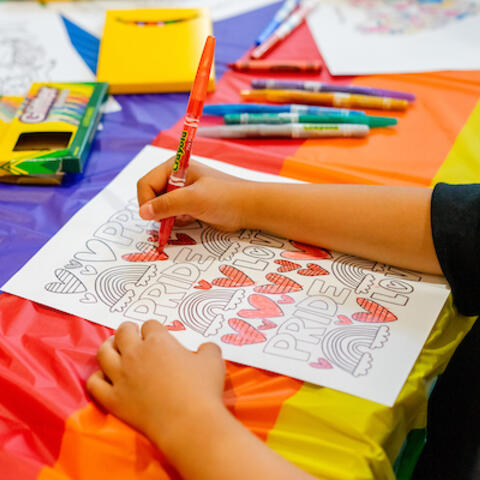 Child coloring in Pride Event picture with crayons surrounding