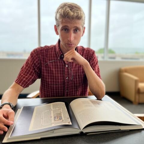 Headshot of Daniel Jacobs; hand on chin with book on desk