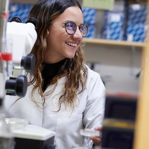 Maria in her lab coat smiling behind equipment