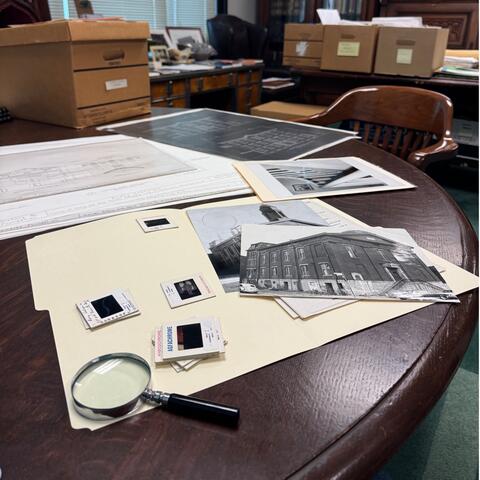 pile of photos and folders with magnifying glass on table