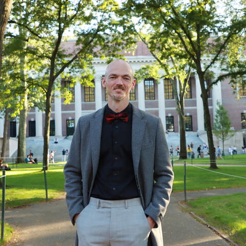Johnny Smith headshot, grey jacket standing in Harvard Yard outside of Widener Library
