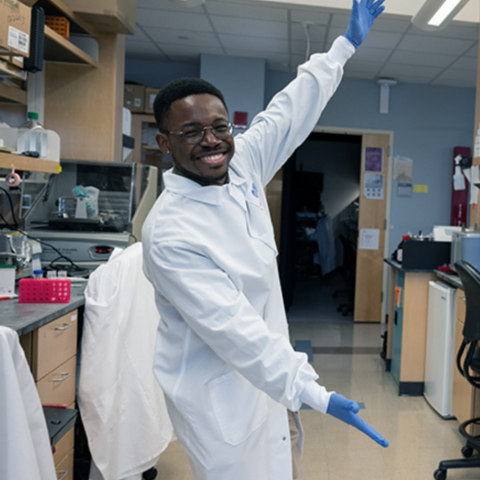 Olúmídé Fagboyegun smiling and gesturing toward his lab equipment