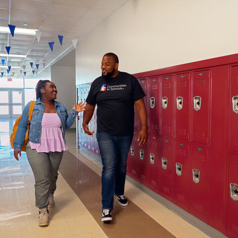 Black male wearing Communities in Schools shirt walking down the hall with a younger Black female