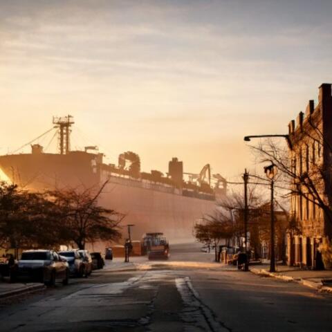 Image representing global trade impact; large ship in the background with goods looking upon a dark city.