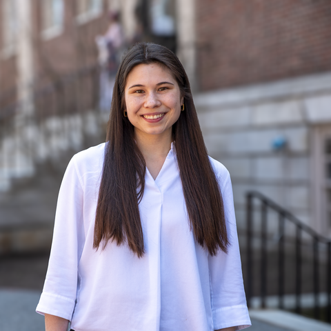 Abigail wearing a white shirt with hair down standing in front of Lehman Hall 
