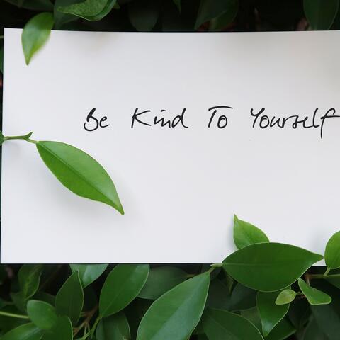 paper that reads, "Be Kind To Yourself" with green leaves around it