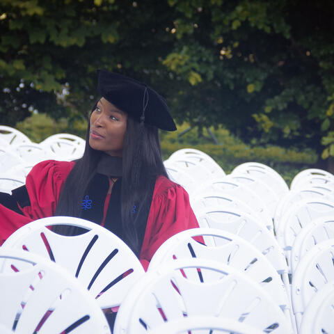 Nkem-Onyekpe sitting in a row of white chairs wearing regalia