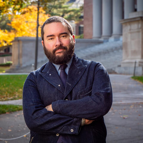 Daniel Evrard headshot; wearing a dark denim jacket standing in front of Widener Library