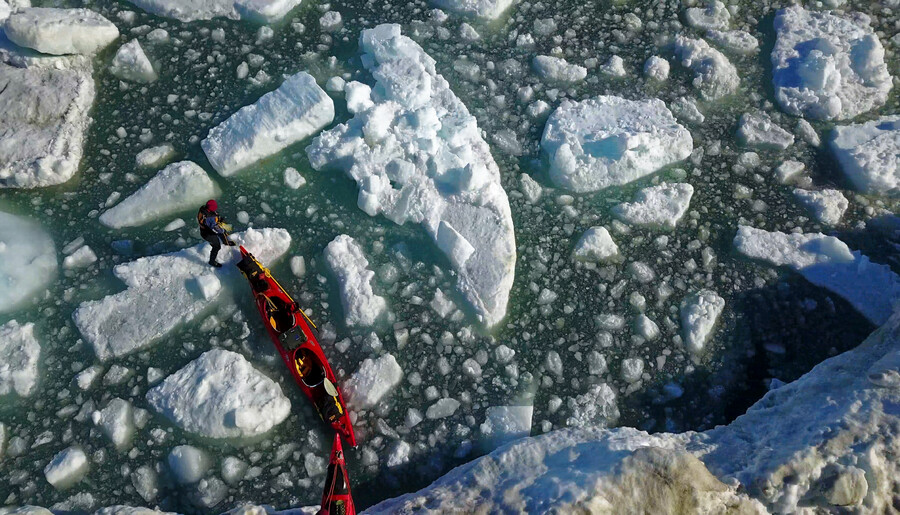 A team pulls red kayaks over ice and water