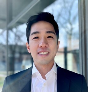 PhD student Sean Lee wearing a white shirt and suit jacket, smiling at the camera.