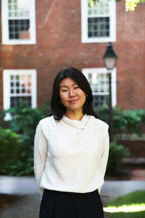 Harvard Griffin GSAS PhD student Fiona Chen standing outside in front of a brick building in a white blouse.