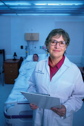 Elizabeth Klerman in white lab coat with arms crossed with bed in back of her.