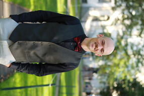 Headshot of Johnny Smith, wearing a black button down with grey vest, standing in Harvard Yard