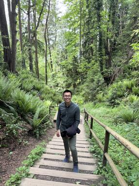 Alan Wong on a trail with greenery forest in the background