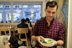 Matthew Hayek, wearing plaid shirt, looks down at a bowl of food in a restaurant