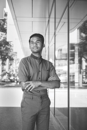 Srujan Meesala, standing with his arms crossed and wearing glasses and a button down shirt with the sleeves rolled up