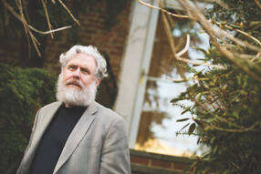 George Church, with a white beard and wearing a blazer, stands outside