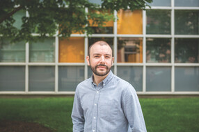 Jacob Moses, wearing a button-down shirt, faces the camera