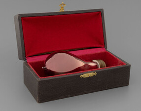 A lightbulb made of red glass is displayed in a wood and red velvet box