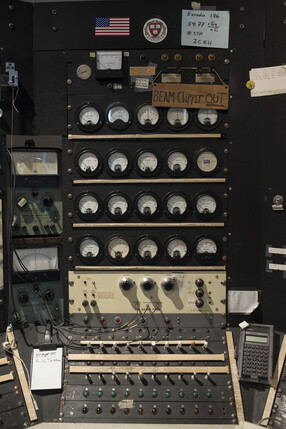 Closeup of cyclotron control panel dials, with handwritten notes, a Harvard shield sticker, and an American flag attached to the controls.