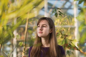Holly Elmore standing in a greenhouse with plants in the background.