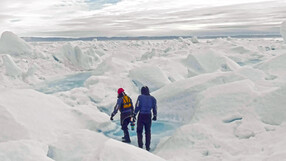 Two people walk across an icy landscape