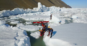 A group of people tries to navigate red kayaks through ice and water.