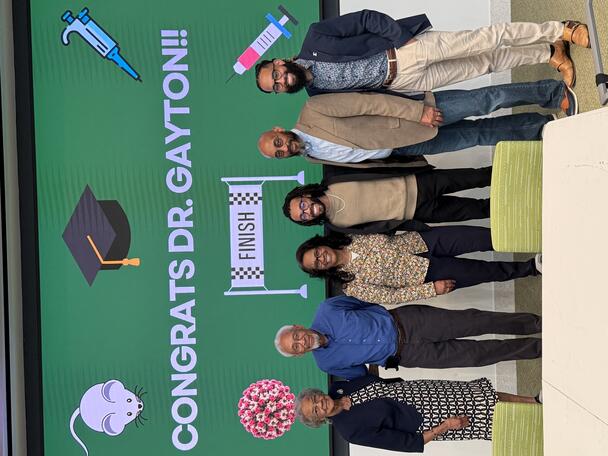 Gayton standing with family members in front of green screen that reads, "Congrats Dr. Gayton"