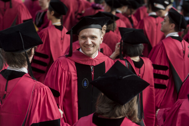 Smiling man stands surrounded by people in red academic robes