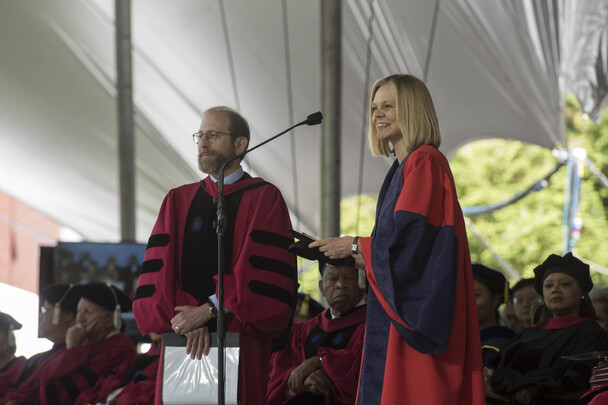 Emma Dench, in academic regalia, stands in front of a microphone