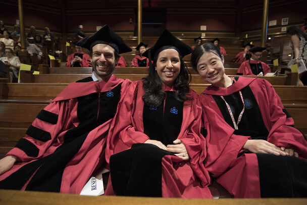 Three students sit in academic robes in Sanders Theatre benches