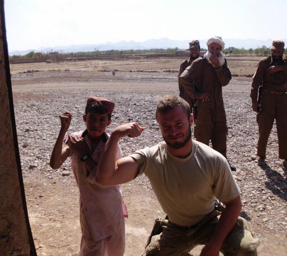 Bellet poses showing arm muscles with Afghan boy and local police